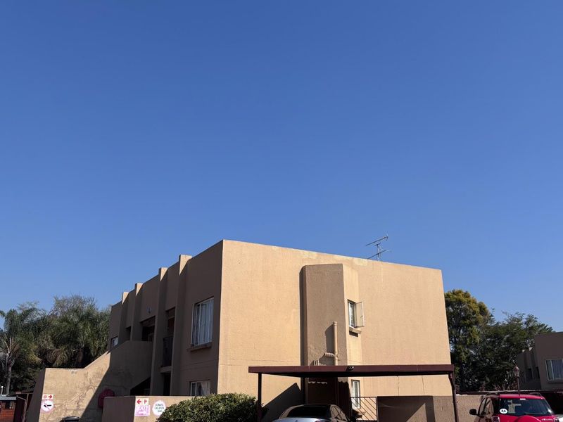 Exterior view of a multi-story apartment complex featuring plastered facades and covered carport parking areas.