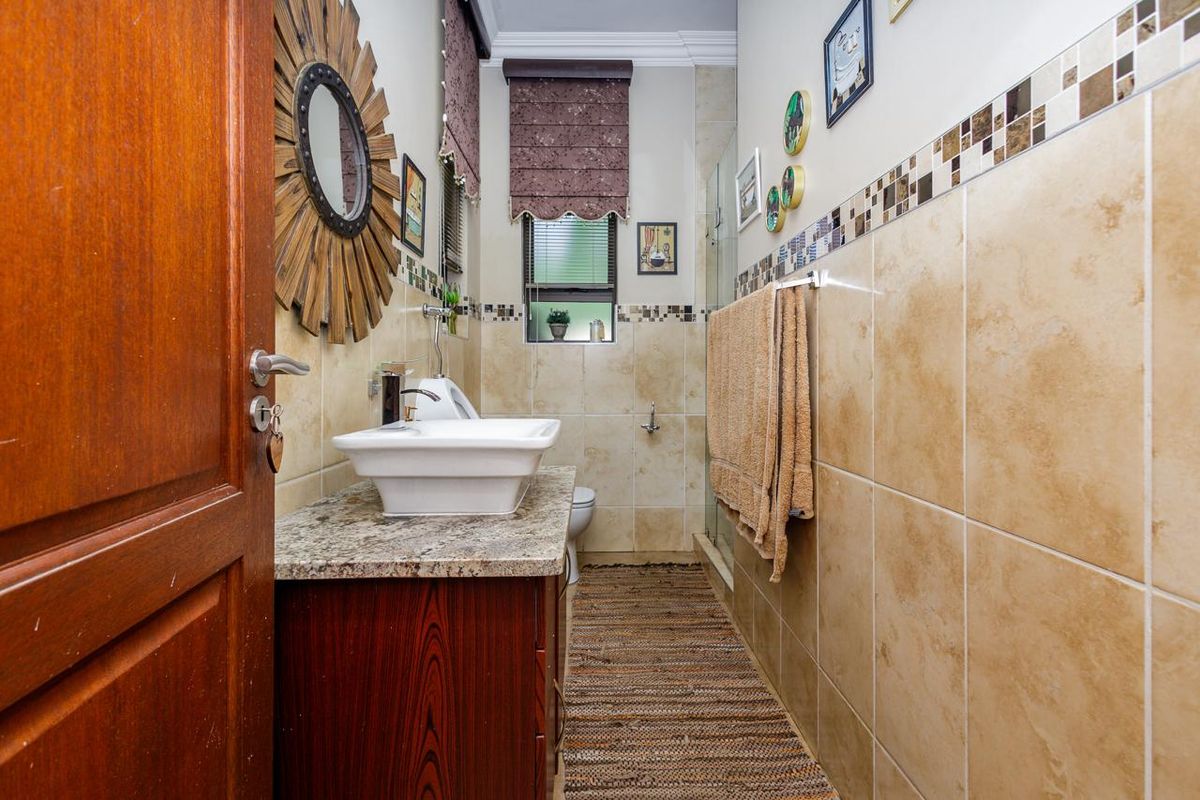 A compact bathroom featuring a vessel sink on a granite vanity, tiled walls with decorative mosaic accents, and a glass-enclosed shower area.