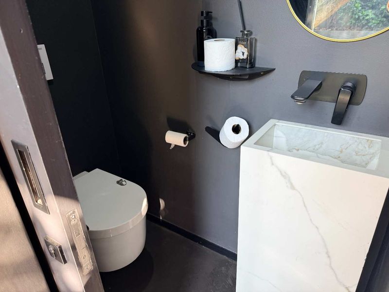 Modern powder room featuring a sleek freestanding marble-look pedestal basin, matte black fixtures, and a wall-mounted toilet against dark charcoal walls.