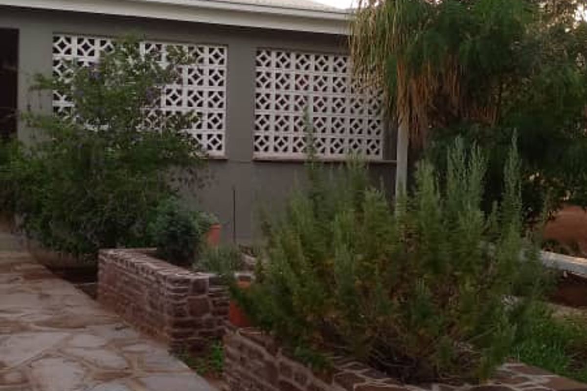 Exterior view of the property featuring a stone-paved walkway, raised brick garden beds, and decorative breeze block wall detailing.