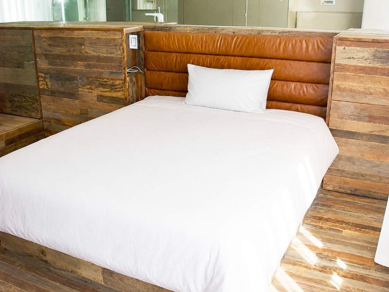 A modern bedroom featuring a custom built-in timber bed frame with an integrated leather headboard and matching wood paneling.