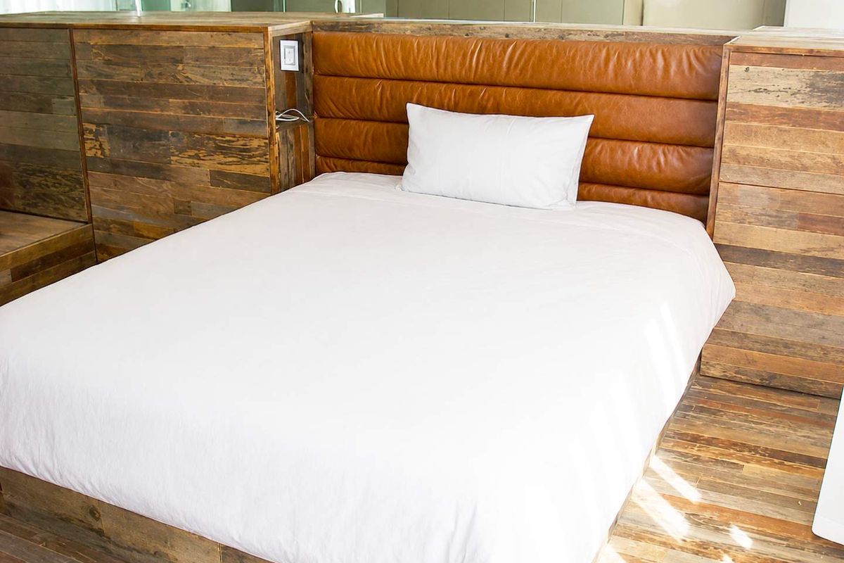 A modern bedroom featuring a custom built-in timber bed frame with an integrated leather headboard and matching wood paneling.