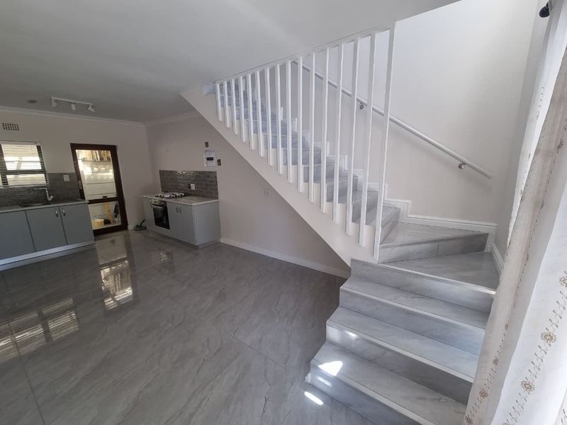 An open-plan living and kitchen area featuring modern grey tiled flooring, a built-in kitchen with integrated appliances, and a white staircase.