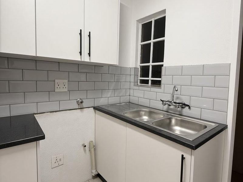 A functional laundry area featuring white cabinetry, a double stainless steel sink, subway tile backsplash, and tiled flooring.