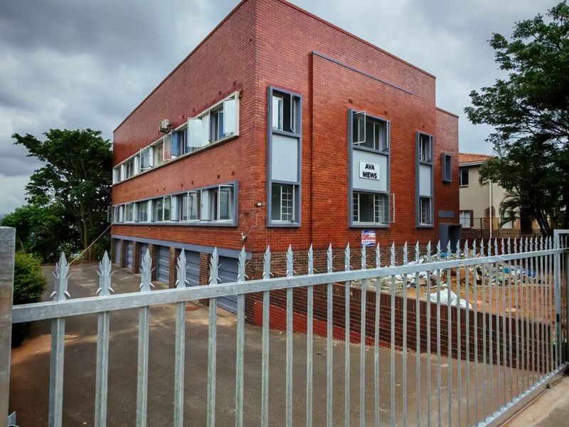 Exterior view of Ava Mews apartment building featuring a red brick facade, metal security fencing, and ground-level garage access.