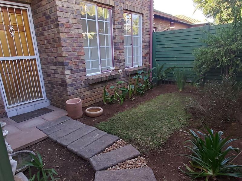 A rear exterior view of a face brick townhouse featuring a small garden area, paved walkway, and secure gated access.