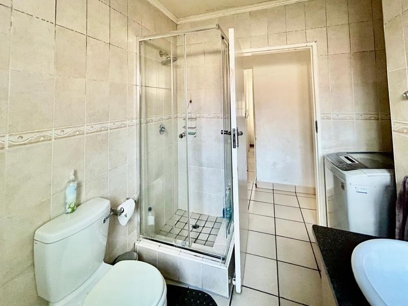A functional bathroom featuring a shower enclosure, toilet, and vanity basin with tiled finishes throughout, requiring some maintenance and cosmetic updates.