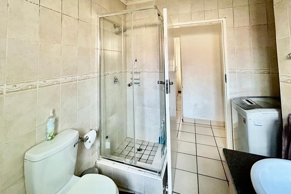 A functional bathroom featuring a shower enclosure, toilet, and vanity basin with tiled finishes throughout, requiring some maintenance and cosmetic updates.