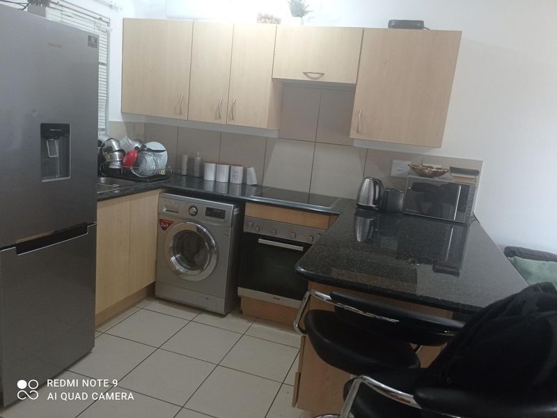 Compact kitchen featuring light wood cabinetry, granite countertops, tiled flooring, and built-in appliances including an oven, hob, and washing machine.