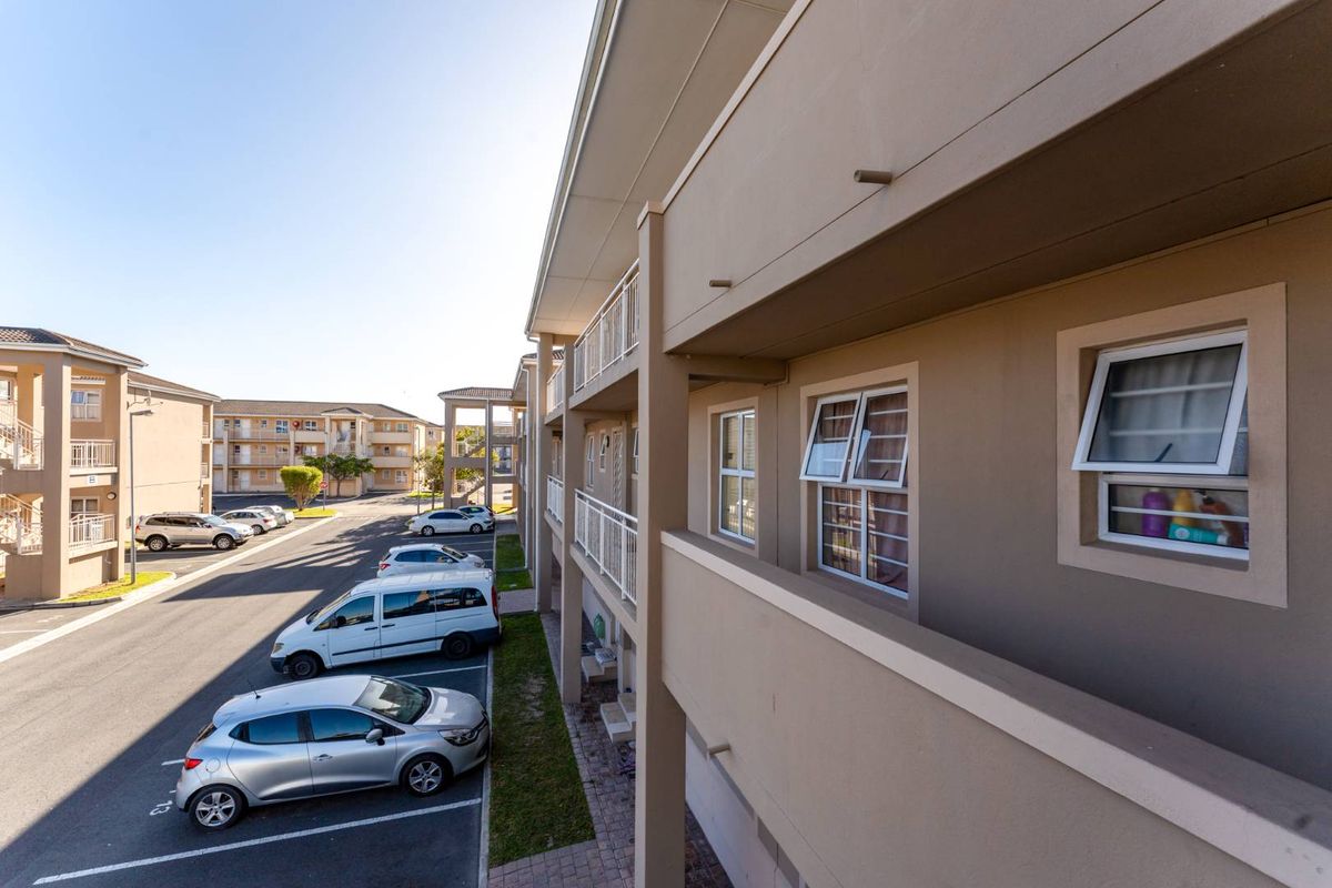 Exterior view of the apartment complex showing the building facade, balcony walkways, and paved parking area.