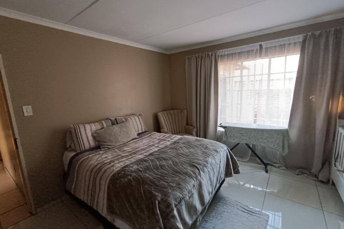 A bedroom featuring tiled flooring, coved ceilings, and a window fitted with security bars, providing a functional and neutral living space.
