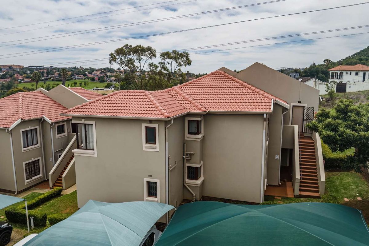 Aerial view of a multi-story apartment complex featuring terracotta tiled roofs, beige exterior walls, and external staircases with shaded parking bays below.