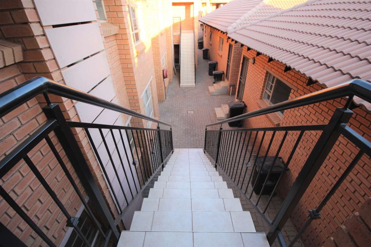 An elevated view looking down a tiled staircase with metal railings into a paved courtyard area between brick apartment buildings.