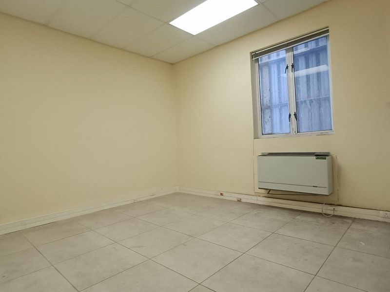 An empty office space featuring tiled flooring, a suspended ceiling, and a wall-mounted HVAC unit.