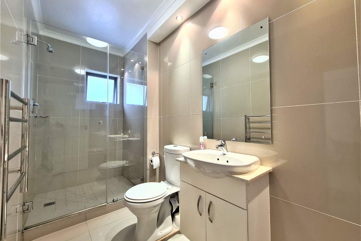 Modern bathroom featuring a glass-enclosed walk-in shower, vanity with integrated basin, wall-mounted mirror, and heated towel rail.