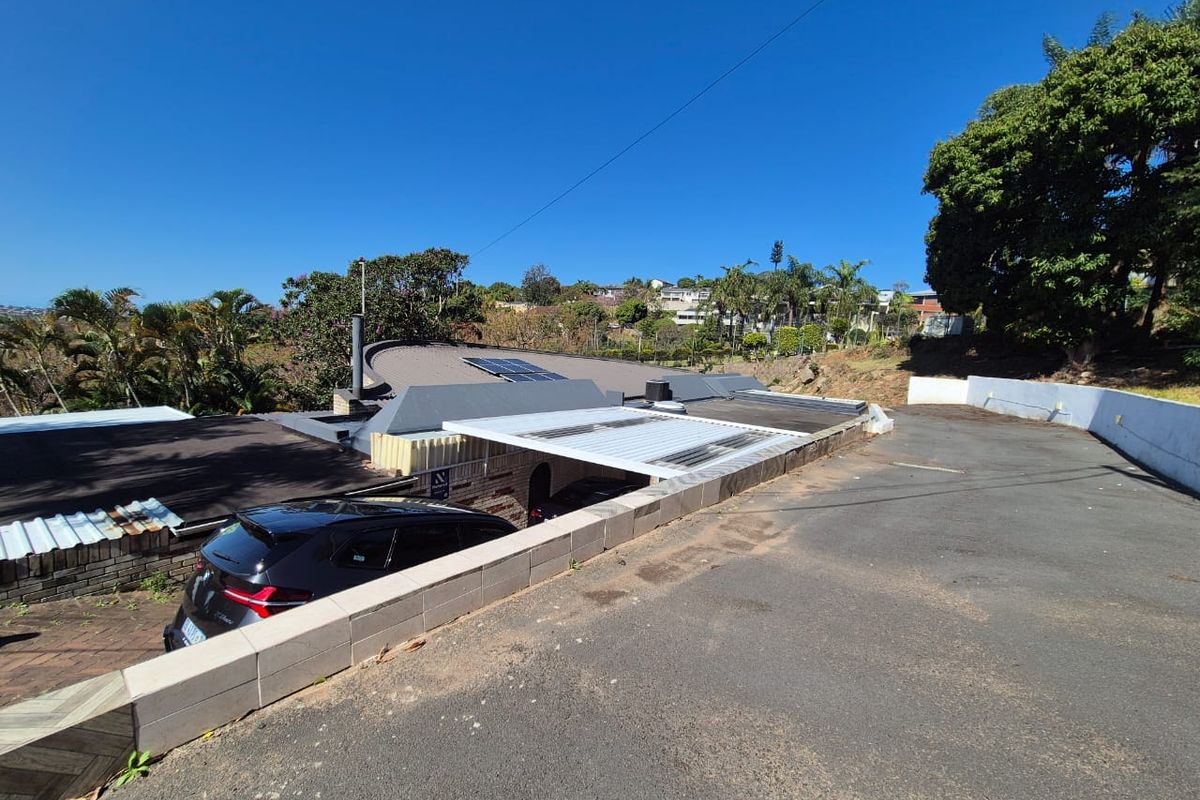 Aerial view of the property showing the driveway, retaining wall, carport structure, and roof with installed solar panels.