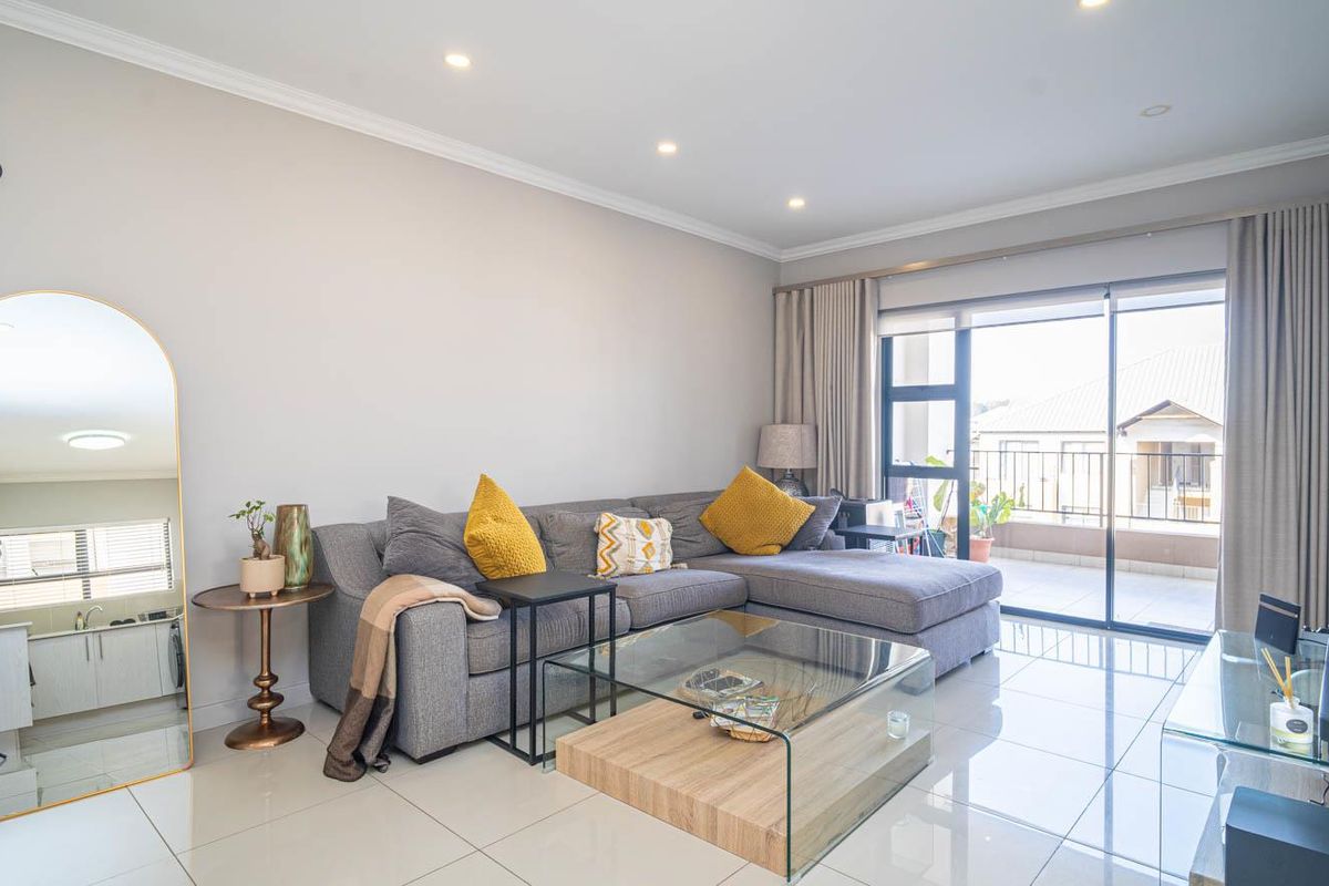 A bright and modern living room featuring large format floor tiles, recessed lighting, and direct access to a private balcony through sliding glass doors.