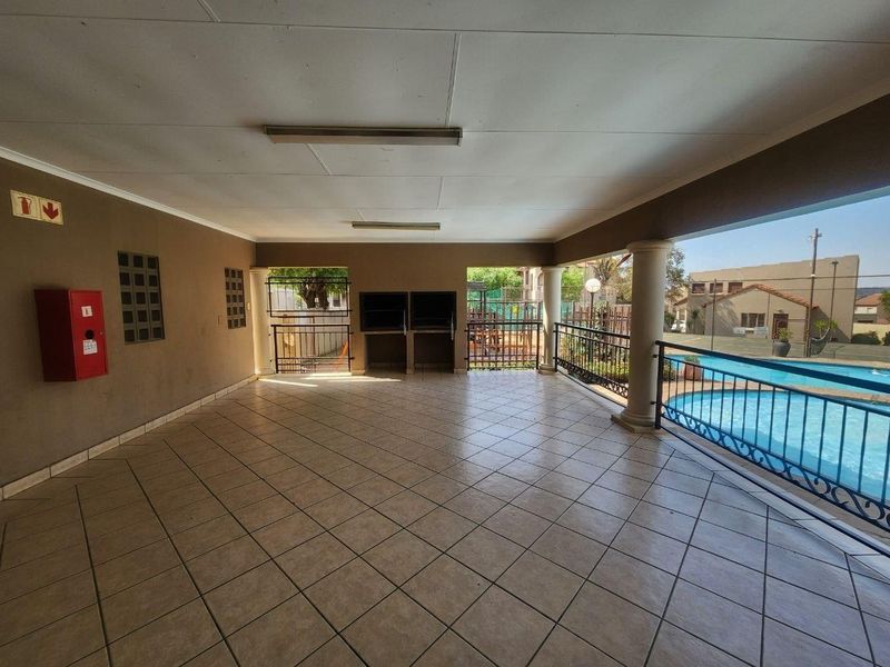 Spacious covered clubhouse area featuring tiled flooring, built-in braai facilities, and direct views overlooking the communal swimming pool.