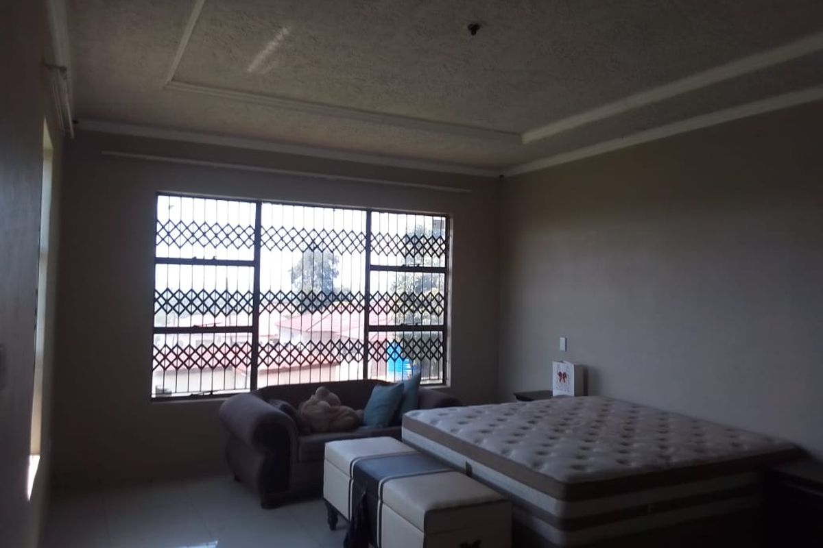 Spacious bedroom featuring tiled flooring, a textured ceiling, and large windows fitted with security bars.