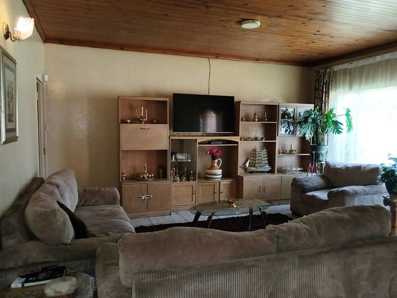 A spacious living room featuring a warm timber tongue and groove ceiling, tiled flooring, and wall-mounted lighting fixtures.