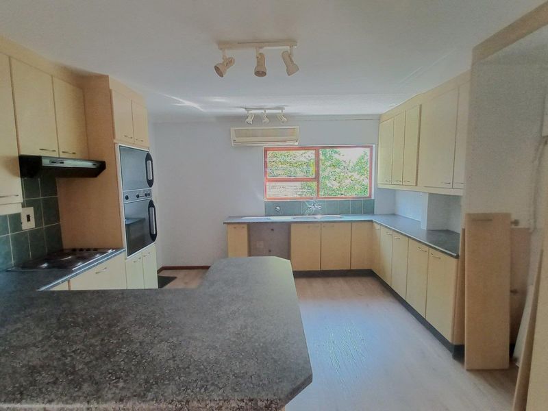 Spacious kitchen featuring light-toned cabinetry, dark laminate countertops, built-in oven, hob, and an integrated air conditioning unit.