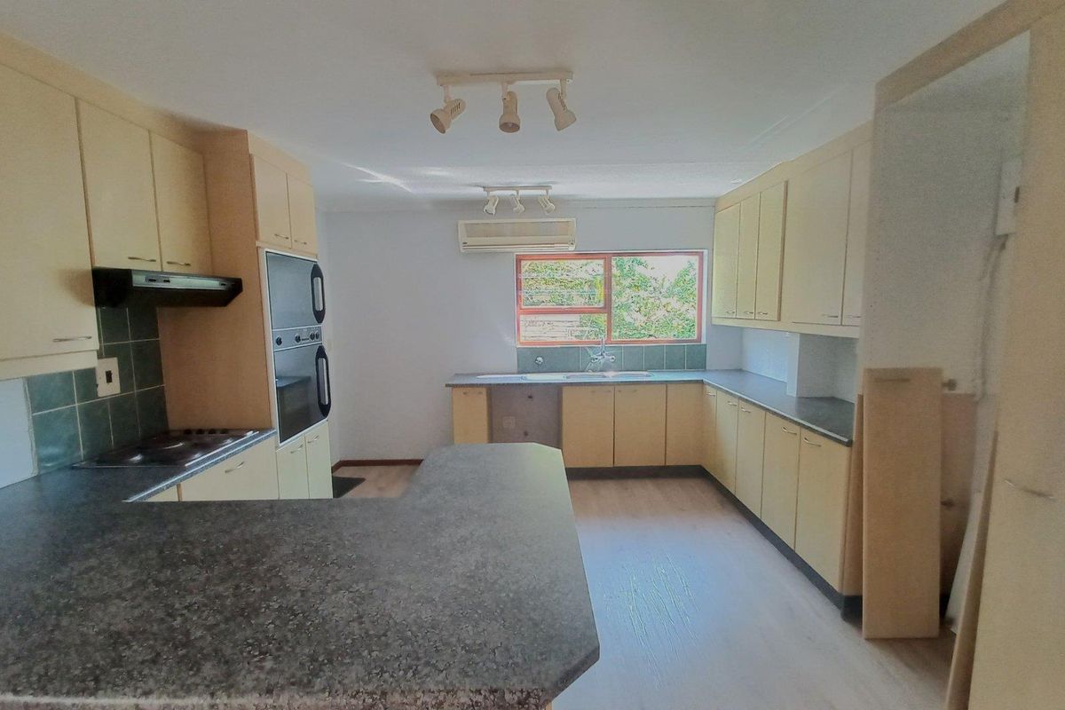 Spacious kitchen featuring light-toned cabinetry, dark laminate countertops, built-in oven, hob, and an integrated air conditioning unit.