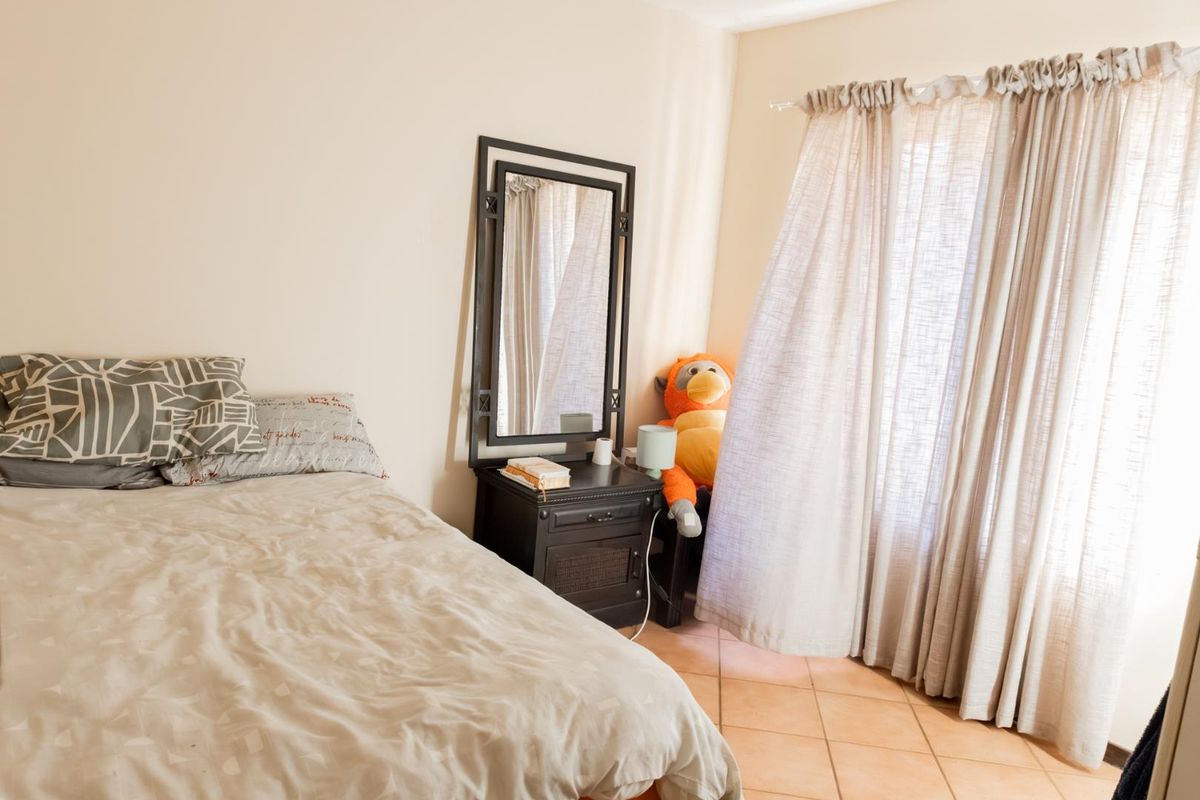 A bedroom featuring tiled flooring and large windows with curtains, providing natural light and a functional living space.