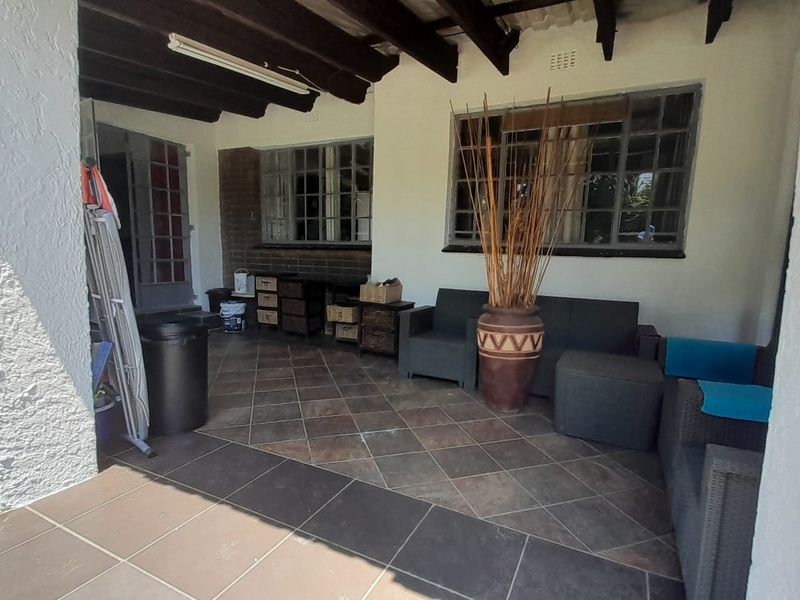 A covered patio area featuring exposed timber ceiling beams, tiled flooring, and steel-framed windows, offering a functional outdoor living space.