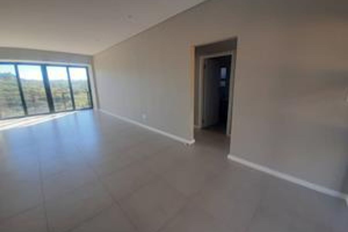A spacious, modern, and empty living area featuring large format floor tiles, recessed lighting, and expansive sliding glass doors leading to an outdoor view.