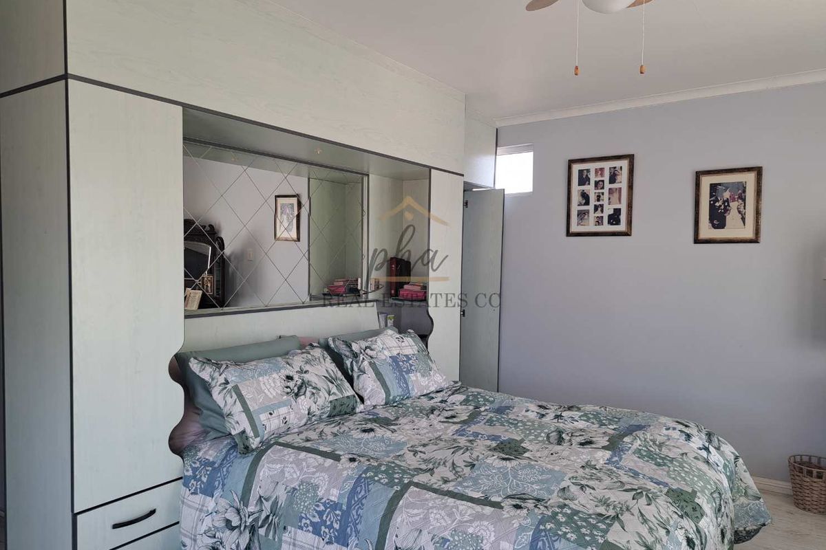 A bedroom featuring built-in cupboards with a mirrored headboard section, a ceiling fan, and laminate flooring.