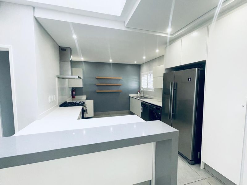 Modern kitchen featuring sleek white cabinetry, stone countertops, a gas hob with extractor, and a functional breakfast bar in a clean, contemporary layout.