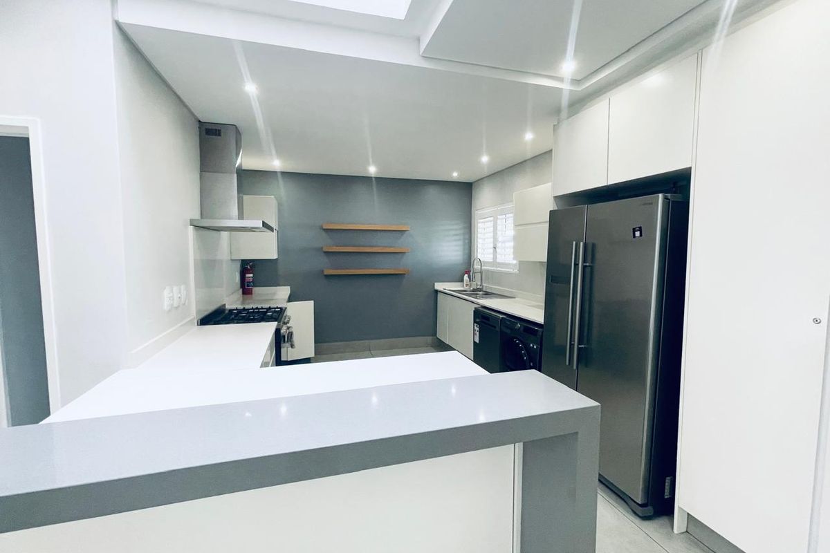 Modern kitchen featuring sleek white cabinetry, stone countertops, a gas hob with extractor, and a functional breakfast bar in a clean, contemporary layout.