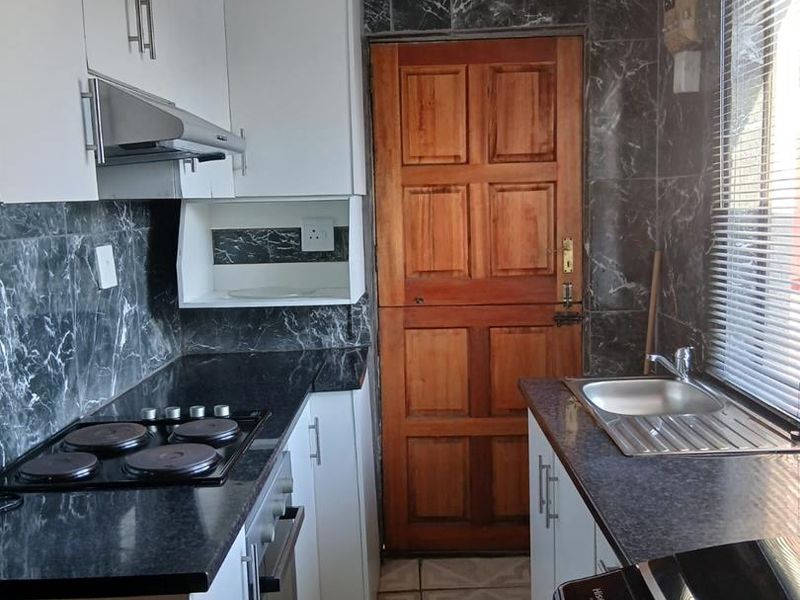 Compact kitchen featuring white cabinetry, dark marble-look wall tiles, built-in oven, electric hob, and a stainless steel sink.