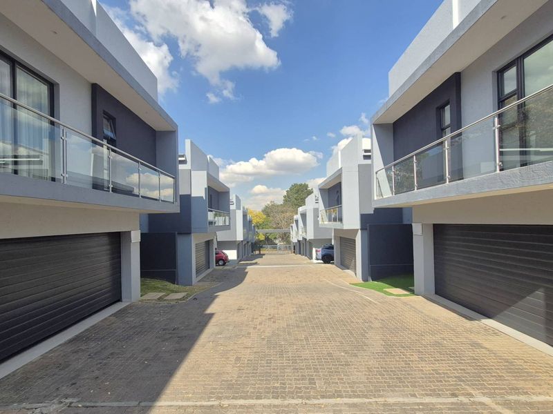 A modern cluster development featuring paved driveway access, automated garages, and upper-level balconies with glass balustrades.