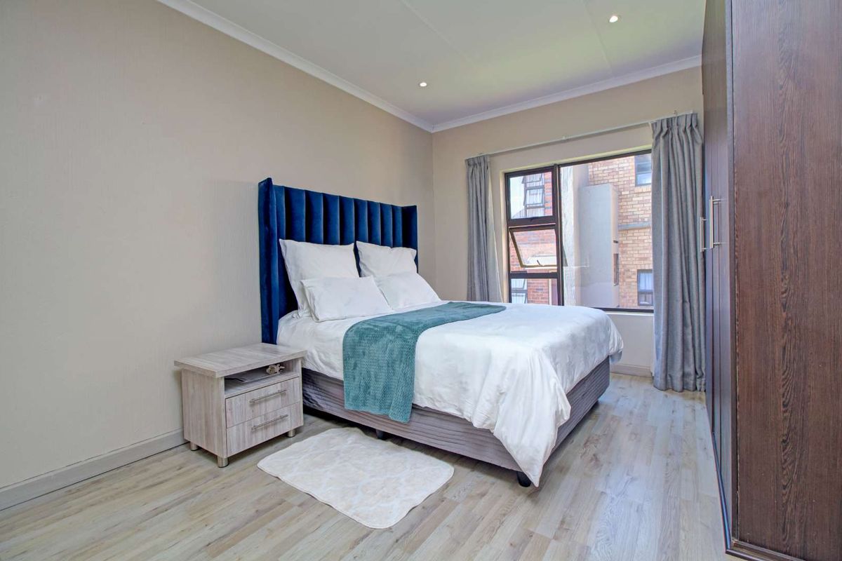 A well-maintained bedroom featuring light wood-look flooring, recessed ceiling lighting, and a large window providing natural light.