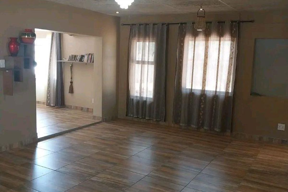 Spacious living area featuring wood-look floor tiles, recessed lighting, and a drop ceiling, with an open transition to an adjacent room.