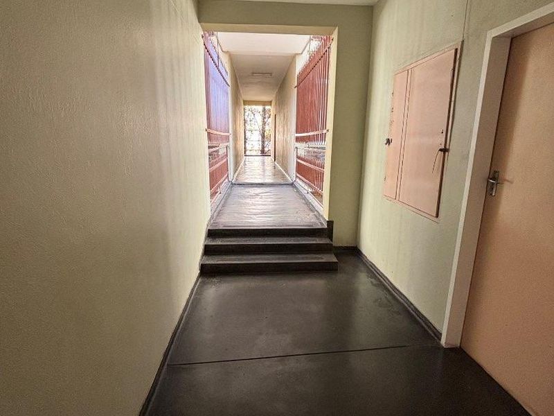 A functional apartment hallway featuring concrete flooring, a built-in utility cabinet, and a metal security gate leading to an outdoor walkway.