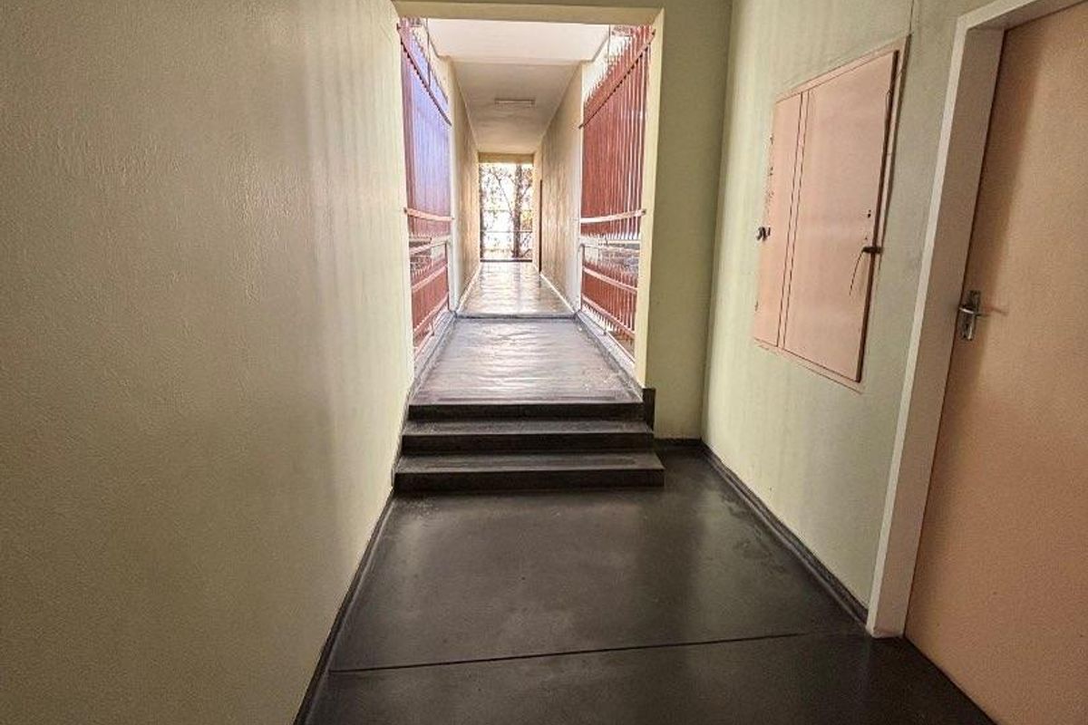 A functional apartment hallway featuring concrete flooring, a built-in utility cabinet, and a metal security gate leading to an outdoor walkway.