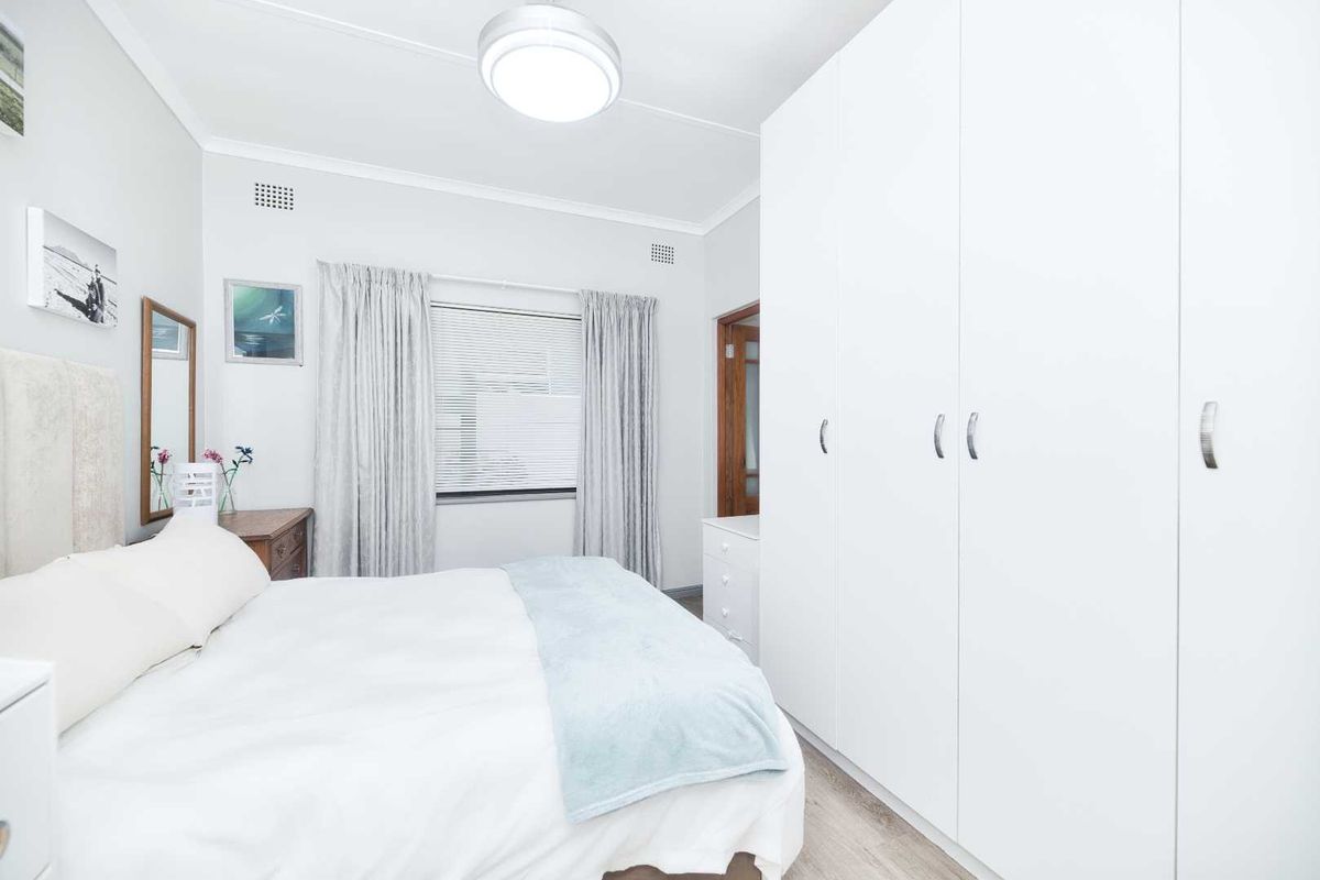 A bright and well-maintained bedroom featuring extensive built-in floor-to-ceiling cupboards, neutral finishes, and natural light through venetian blinds.