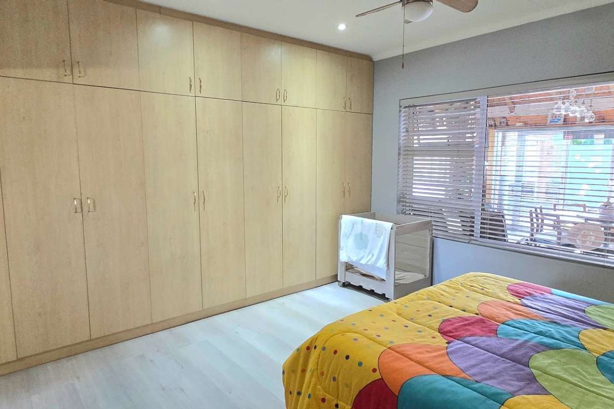 Spacious bedroom featuring extensive floor-to-ceiling built-in wooden cabinetry, light-toned flooring, and large windows with fitted blinds.