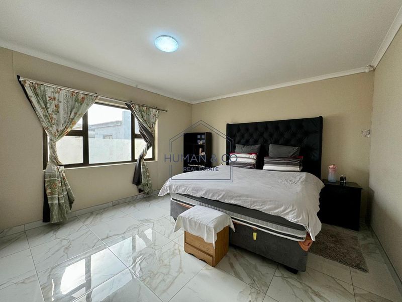 A spacious bedroom featuring large-format marble-look floor tiles, neutral wall tones, and a large window providing natural light.