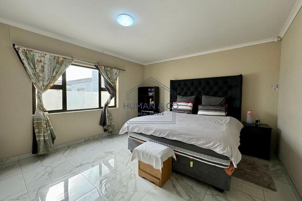A spacious bedroom featuring large-format marble-look floor tiles, neutral wall tones, and a large window providing natural light.