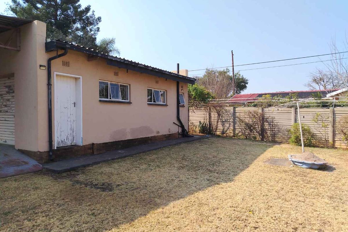 Rear view of the property featuring a modest garden, concrete boundary wall, and exterior access door to the main structure.