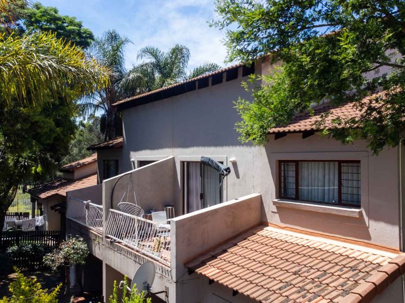 Rear elevation of the apartment building featuring a private balcony with metal railings, terracotta roof tiles, and mature surrounding trees.