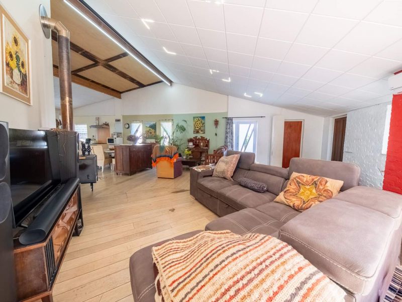 Spacious open-plan living area featuring timber flooring, exposed ceiling beams, a wood-burning stove, and a split-system air conditioner.