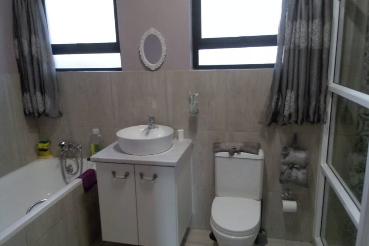 A functional bathroom featuring a vessel sink on a vanity cabinet, a bathtub, and a toilet with neutral wall tiling and aluminium window frames.