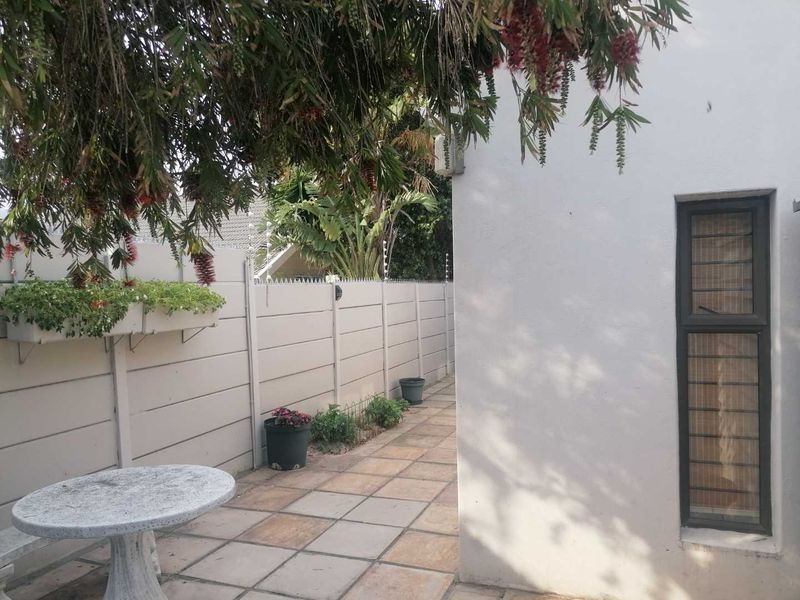 A paved rear patio area featuring a precast concrete boundary wall with security spikes and a window with fitted security bars.