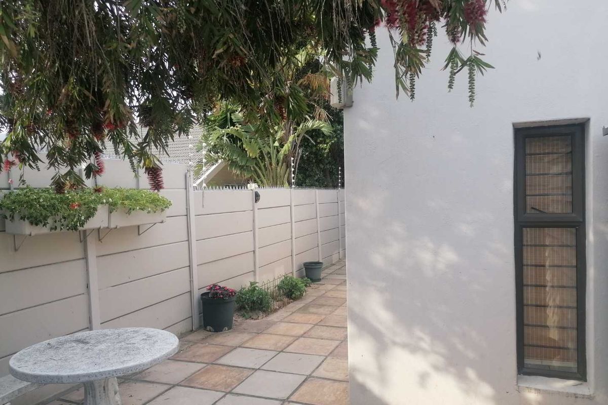 A paved rear patio area featuring a precast concrete boundary wall with security spikes and a window with fitted security bars.
