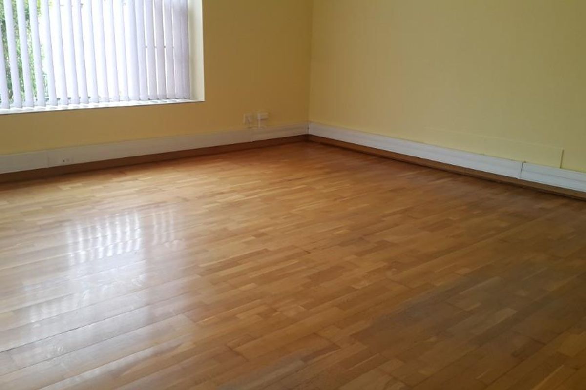 An empty room featuring polished parquet wood flooring, vertical blinds, and neutral yellow walls, offering a versatile space ready for customization.