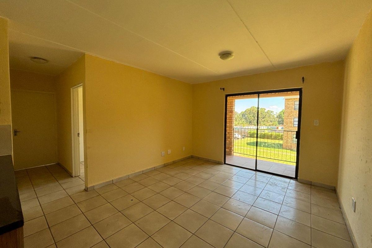 An empty living area featuring tiled flooring and a sliding glass door that opens onto a balcony with exterior views.